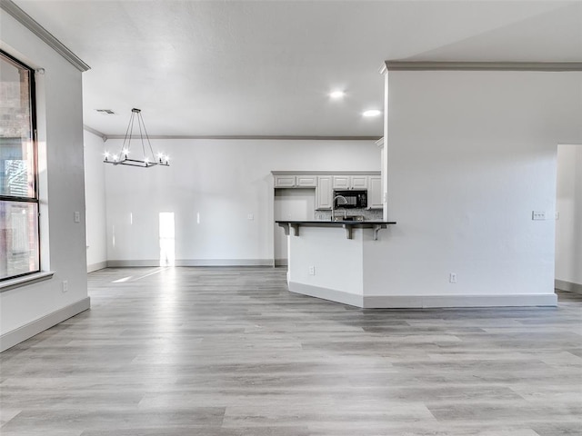 unfurnished living room featuring light hardwood / wood-style flooring, crown molding, plenty of natural light, and an inviting chandelier