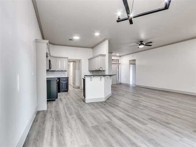 kitchen featuring a breakfast bar area, ceiling fan, gray cabinetry, tasteful backsplash, and light wood-type flooring