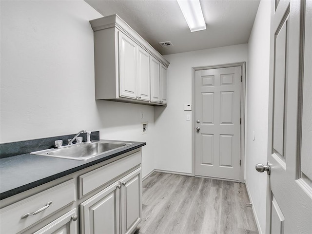 washroom featuring sink, hookup for a washing machine, cabinets, and light wood-type flooring