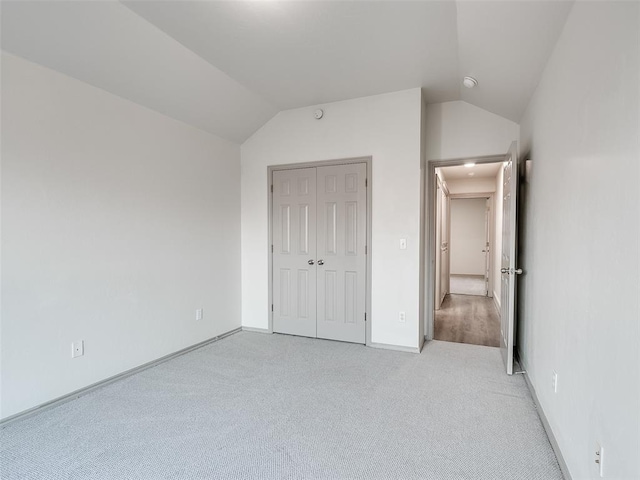 unfurnished bedroom with vaulted ceiling, light carpet, and a closet