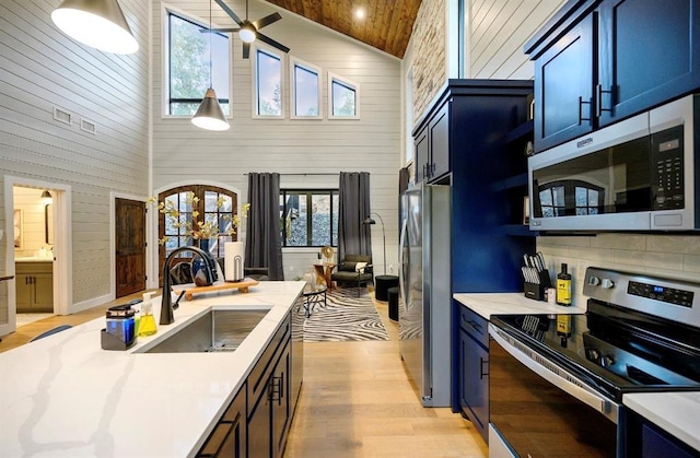 kitchen with appliances with stainless steel finishes, blue cabinets, sink, and light hardwood / wood-style flooring