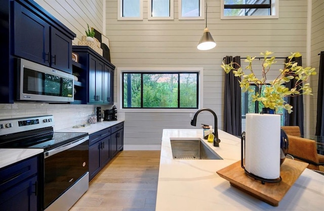 kitchen with blue cabinetry, stainless steel appliances, sink, and hanging light fixtures