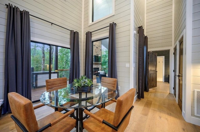 dining room with a towering ceiling, a fireplace, light hardwood / wood-style floors, and wood walls