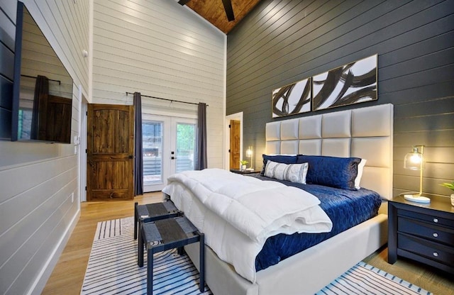 bedroom featuring french doors, light wood-type flooring, access to outside, wooden walls, and a towering ceiling