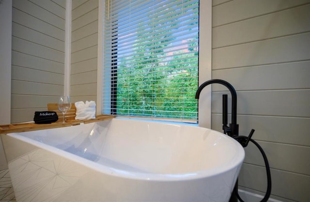 bathroom featuring a healthy amount of sunlight, a washtub, and wooden walls