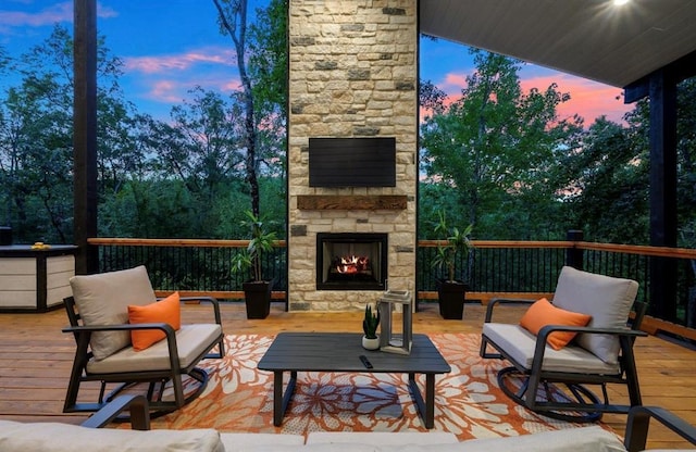 deck at dusk featuring an outdoor stone fireplace