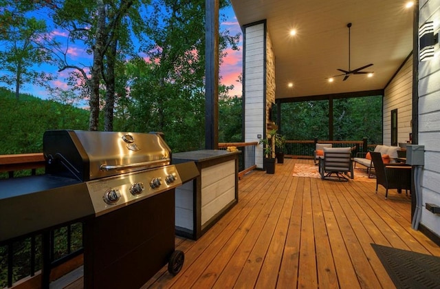 deck at dusk with exterior kitchen, grilling area, an outdoor living space, and ceiling fan