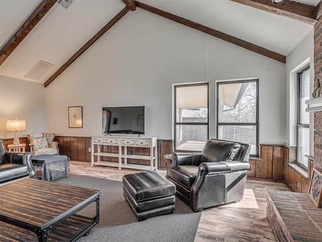 living room with beamed ceiling, light wood-type flooring, high vaulted ceiling, and wood walls