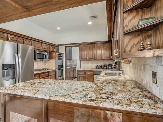 kitchen featuring tasteful backsplash, sink, light stone counters, kitchen peninsula, and stainless steel appliances