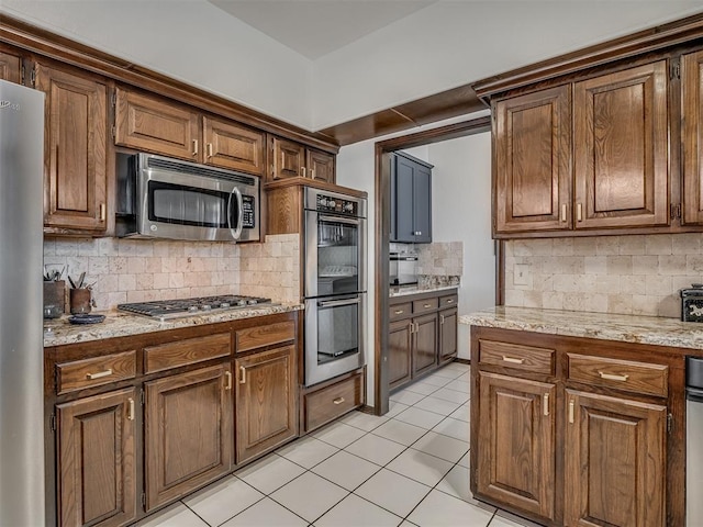 kitchen with light stone counters, stainless steel appliances, tasteful backsplash, and light tile patterned floors