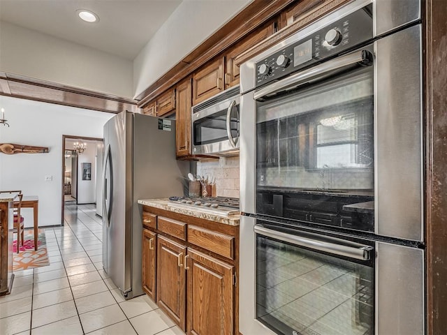 kitchen featuring an inviting chandelier, stainless steel appliances, light tile patterned floors, and backsplash