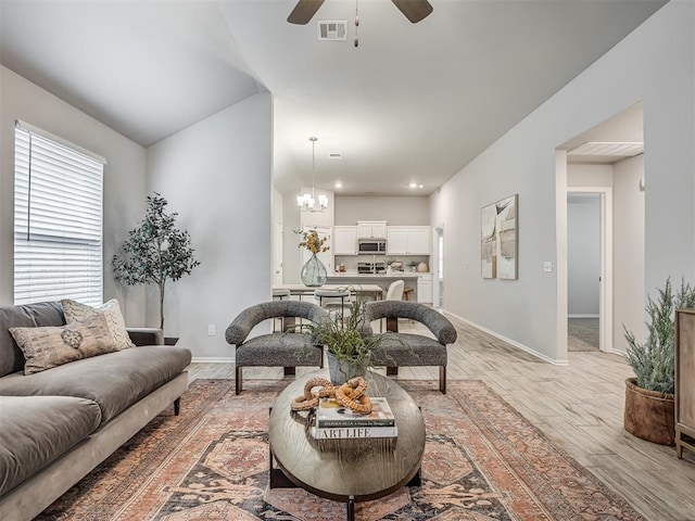 living room featuring ceiling fan with notable chandelier and light wood-type flooring