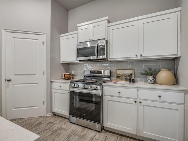 kitchen with white cabinetry, appliances with stainless steel finishes, backsplash, and light wood-type flooring