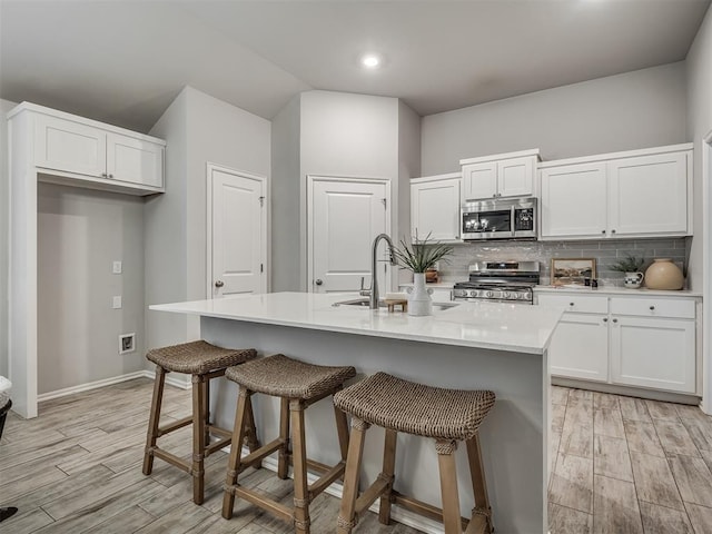 kitchen featuring a kitchen island with sink, sink, stainless steel appliances, and white cabinets