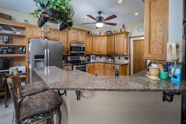 kitchen featuring appliances with stainless steel finishes, a breakfast bar, kitchen peninsula, and dark stone counters