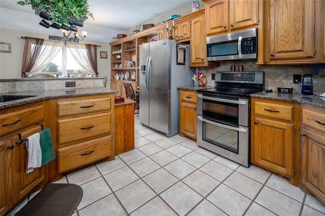 kitchen featuring appliances with stainless steel finishes, decorative backsplash, dark stone counters, light tile patterned floors, and a notable chandelier