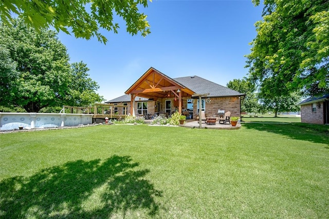 rear view of property featuring a patio, a yard, and an outdoor fire pit