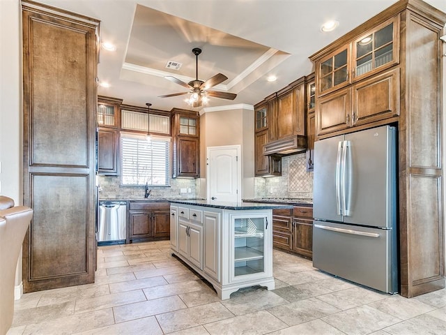 kitchen featuring sink, stainless steel appliances, a kitchen island, a raised ceiling, and dark stone counters