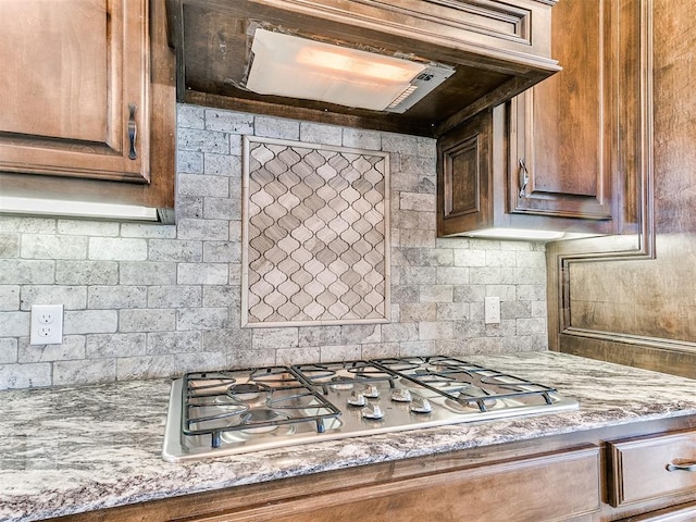 kitchen featuring tasteful backsplash, light stone countertops, custom range hood, and stainless steel gas stovetop