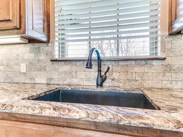 interior details featuring sink, backsplash, and light stone countertops