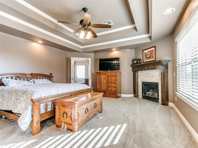 bedroom with a tile fireplace, light colored carpet, ceiling fan, and a tray ceiling