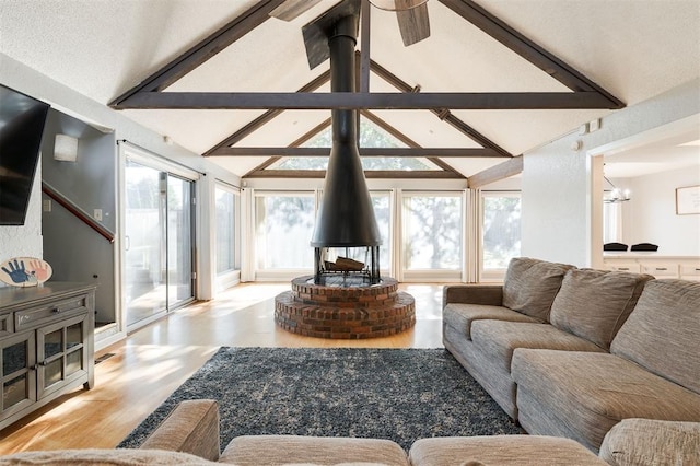 living room with vaulted ceiling with beams, light hardwood / wood-style floors, an inviting chandelier, and a wood stove