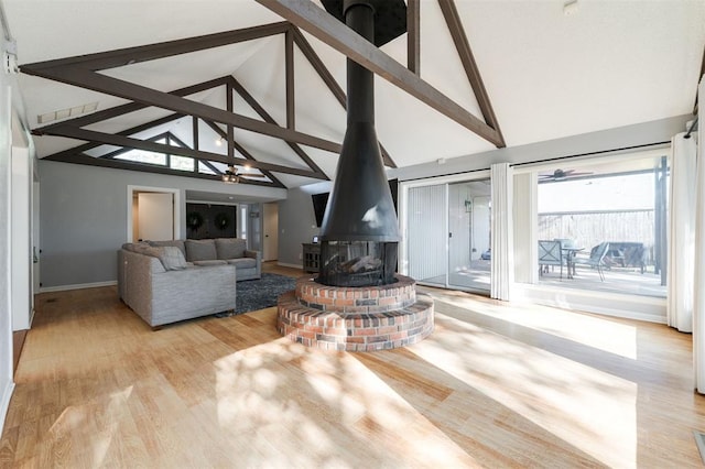 living room featuring high vaulted ceiling, beam ceiling, light hardwood / wood-style floors, and a wood stove