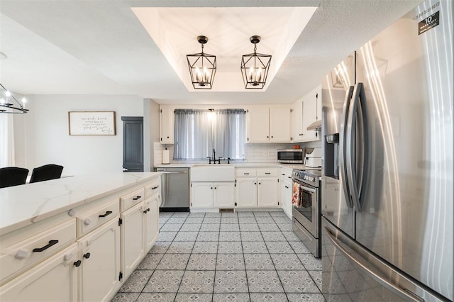 kitchen with a notable chandelier, a tray ceiling, decorative light fixtures, and appliances with stainless steel finishes