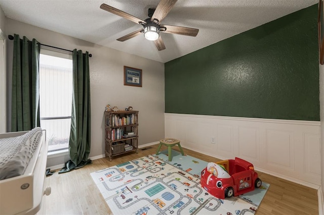 recreation room featuring hardwood / wood-style flooring, ceiling fan, and a textured ceiling