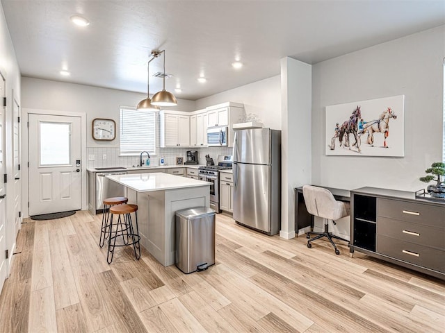 kitchen featuring sink, appliances with stainless steel finishes, white cabinets, a kitchen island, and decorative light fixtures