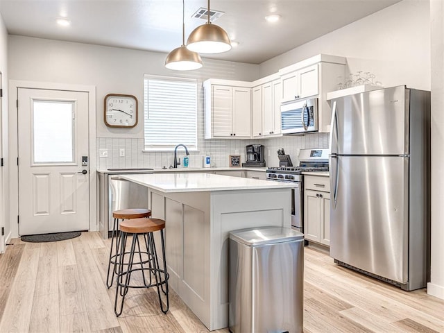 kitchen featuring appliances with stainless steel finishes, white cabinetry, hanging light fixtures, a center island, and light hardwood / wood-style flooring