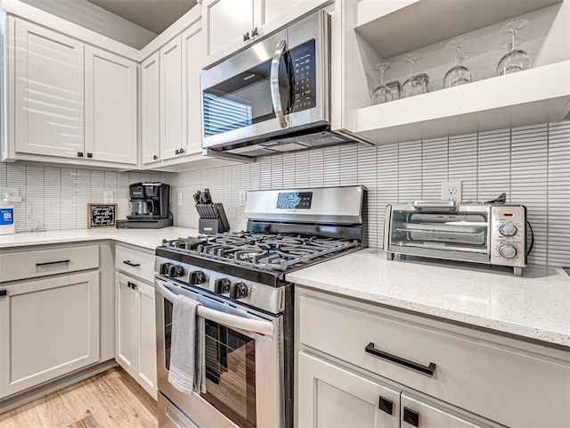 kitchen featuring appliances with stainless steel finishes, tasteful backsplash, white cabinets, light stone counters, and light hardwood / wood-style flooring