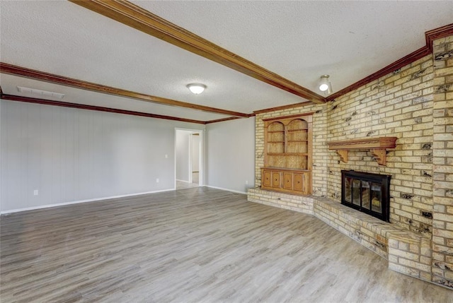 unfurnished living room with hardwood / wood-style floors, a fireplace, a textured ceiling, beam ceiling, and built in shelves