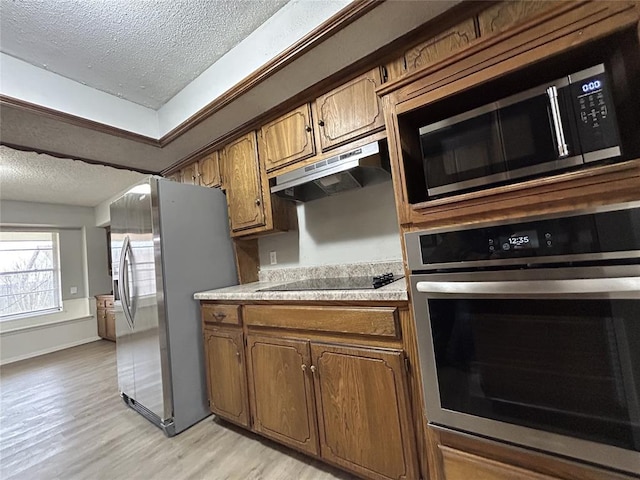 kitchen with stainless steel appliances, a textured ceiling, and light hardwood / wood-style floors