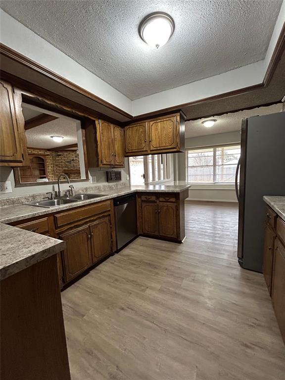 kitchen with sink, light hardwood / wood-style flooring, a textured ceiling, appliances with stainless steel finishes, and kitchen peninsula