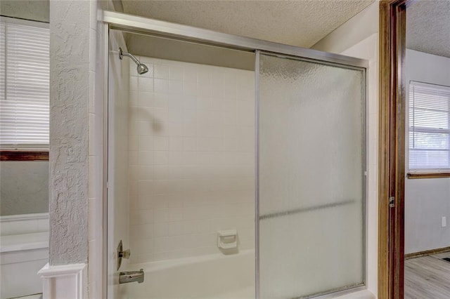 bathroom with hardwood / wood-style flooring, combined bath / shower with glass door, and a textured ceiling