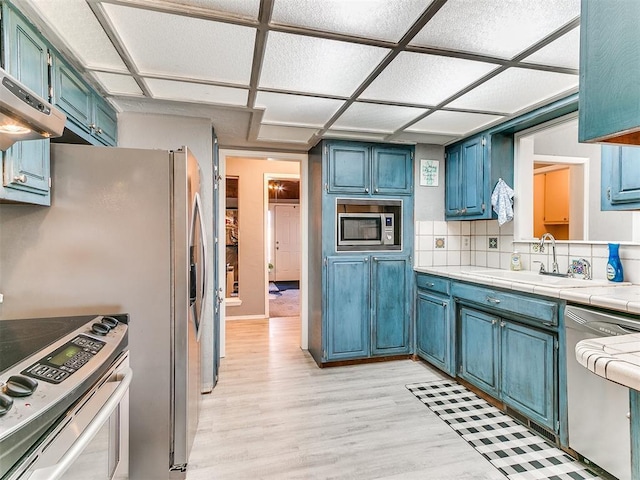 kitchen with sink, tasteful backsplash, light wood-type flooring, appliances with stainless steel finishes, and tile counters