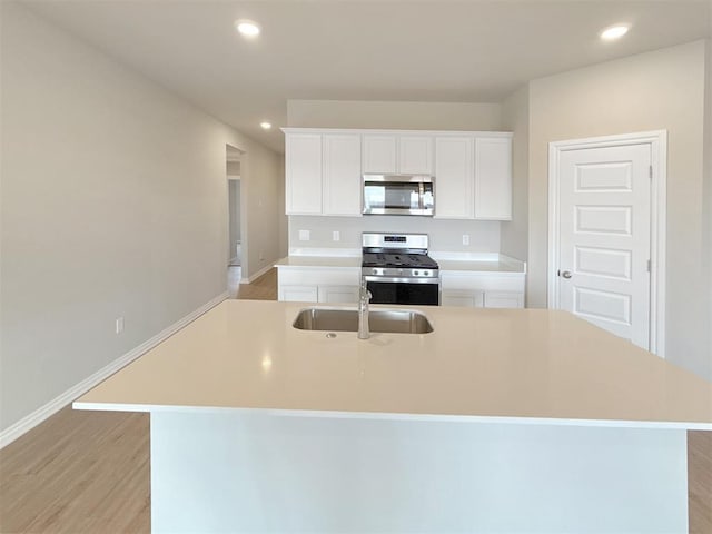 kitchen featuring an island with sink, sink, white cabinets, light hardwood / wood-style floors, and stainless steel appliances