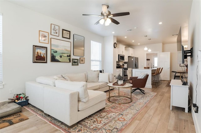 living room with ceiling fan, sink, and light wood-type flooring