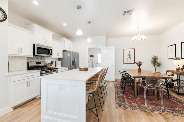 kitchen featuring white cabinetry, stainless steel appliances, decorative light fixtures, and an island with sink