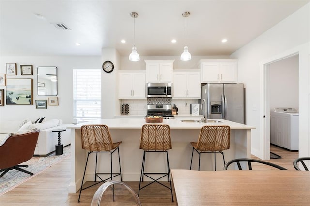 kitchen with sink, appliances with stainless steel finishes, white cabinets, a kitchen bar, and washer / dryer