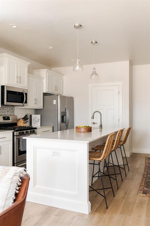 kitchen with stainless steel appliances, hanging light fixtures, a center island with sink, and white cabinets