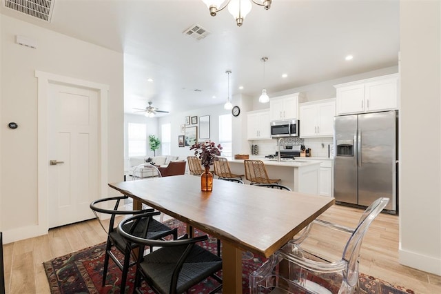 dining space featuring ceiling fan with notable chandelier and light wood-type flooring