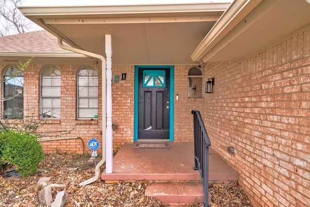 view of exterior entry with brick siding and roof with shingles