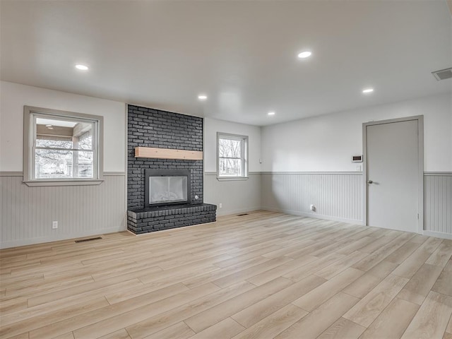 unfurnished living room featuring a brick fireplace and light wood-type flooring