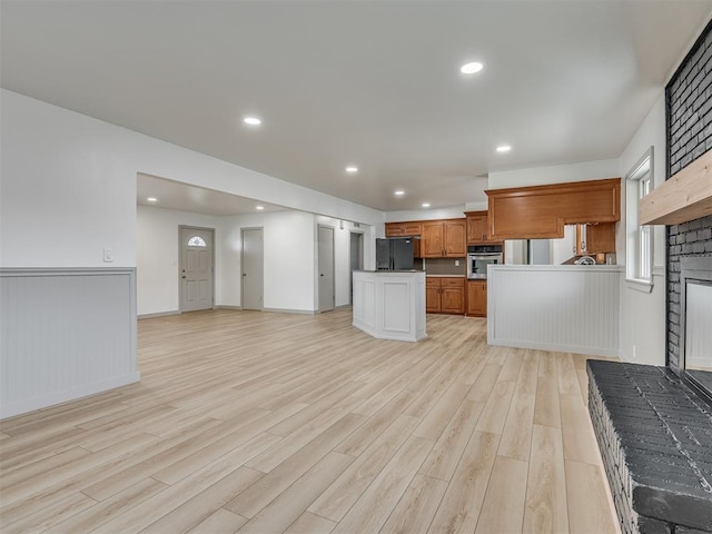 kitchen featuring a center island, black refrigerator with ice dispenser, light wood-type flooring, a fireplace, and oven