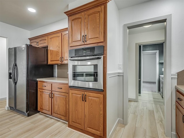 kitchen featuring stainless steel oven, black fridge with ice dispenser, and light hardwood / wood-style floors