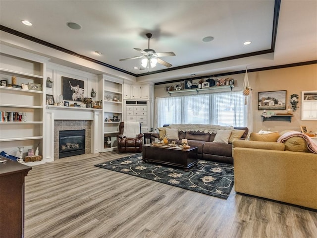 living room with ceiling fan, a fireplace, light wood-type flooring, and a raised ceiling