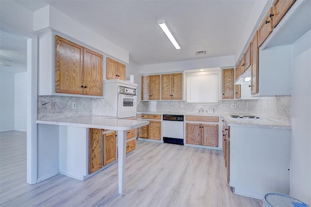 kitchen with white appliances, a kitchen breakfast bar, decorative backsplash, kitchen peninsula, and light wood-type flooring