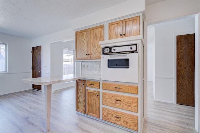 kitchen featuring light brown cabinetry, light hardwood / wood-style floors, white oven, and backsplash